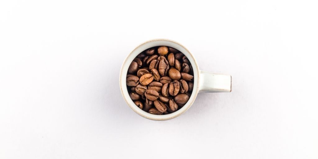 Small espresso mug filled with roasted coffee beans