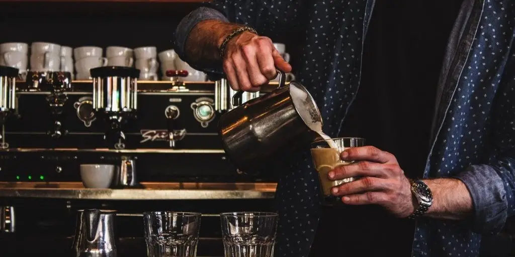 Barista steaming milk and pouring into coffee