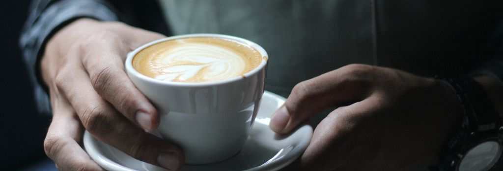 person holding coffee with heart milk design