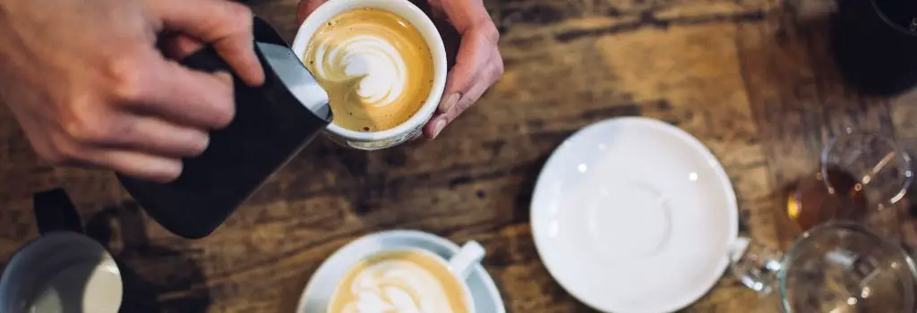 barista pouring milk into coffee making a pattern