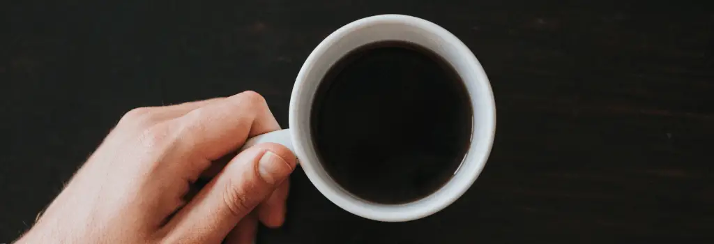 holding strong black coffee in white mug