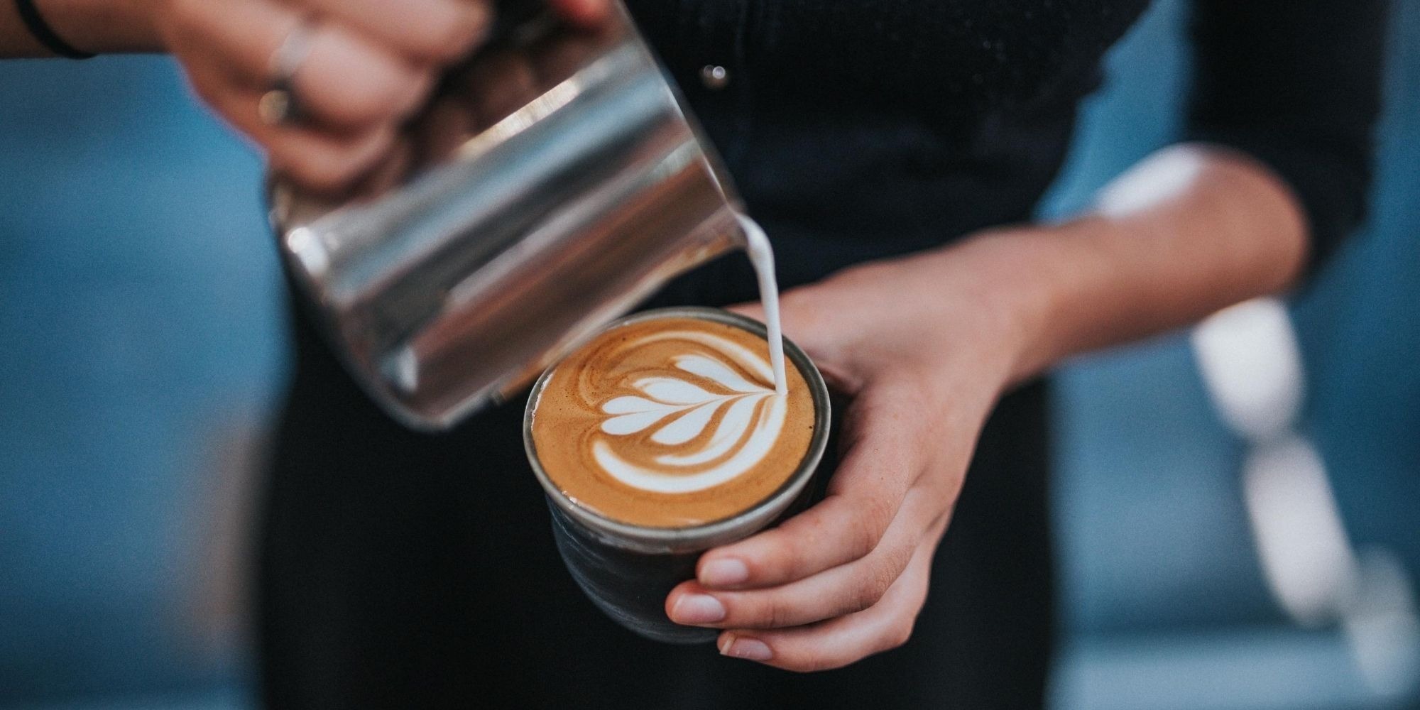 Person pouring milk into flat white coffee