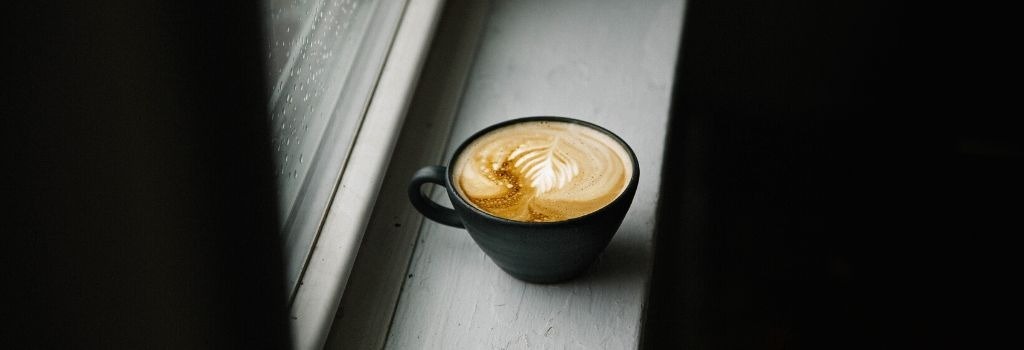 a brewed flat white coffee sitting on the window sill, latte art